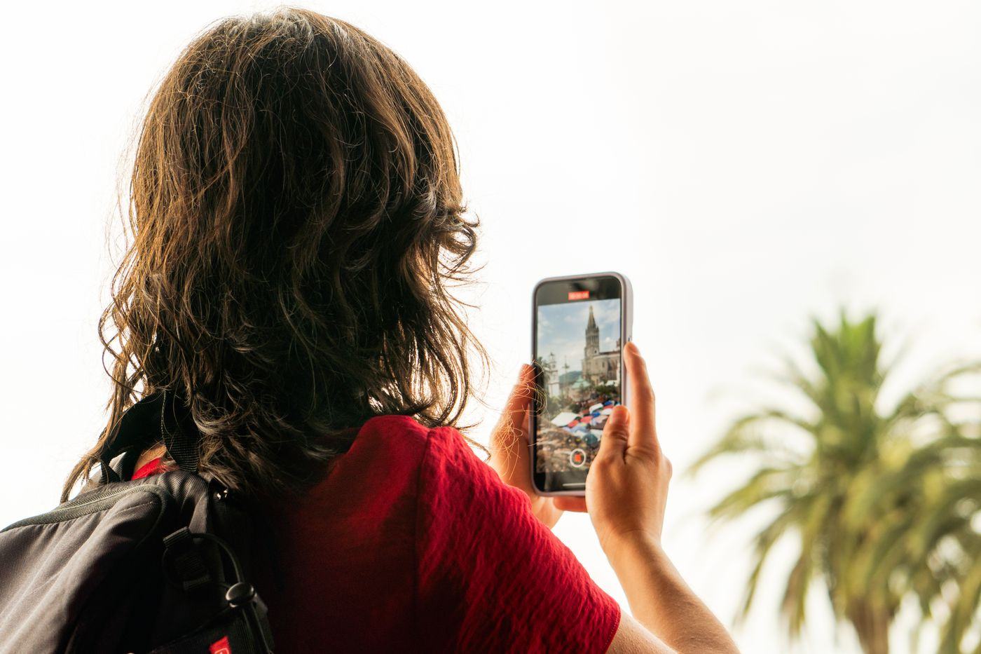 A traveller checking her phone with a backpack on, outside an arrivals hall